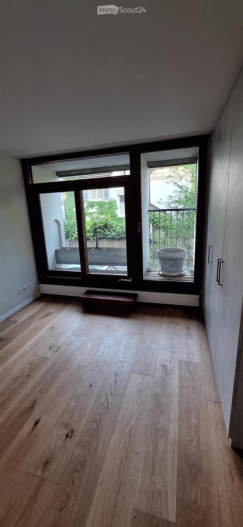 Empty hallway with wooden flooring, large windows, and a small bench near the entrance.