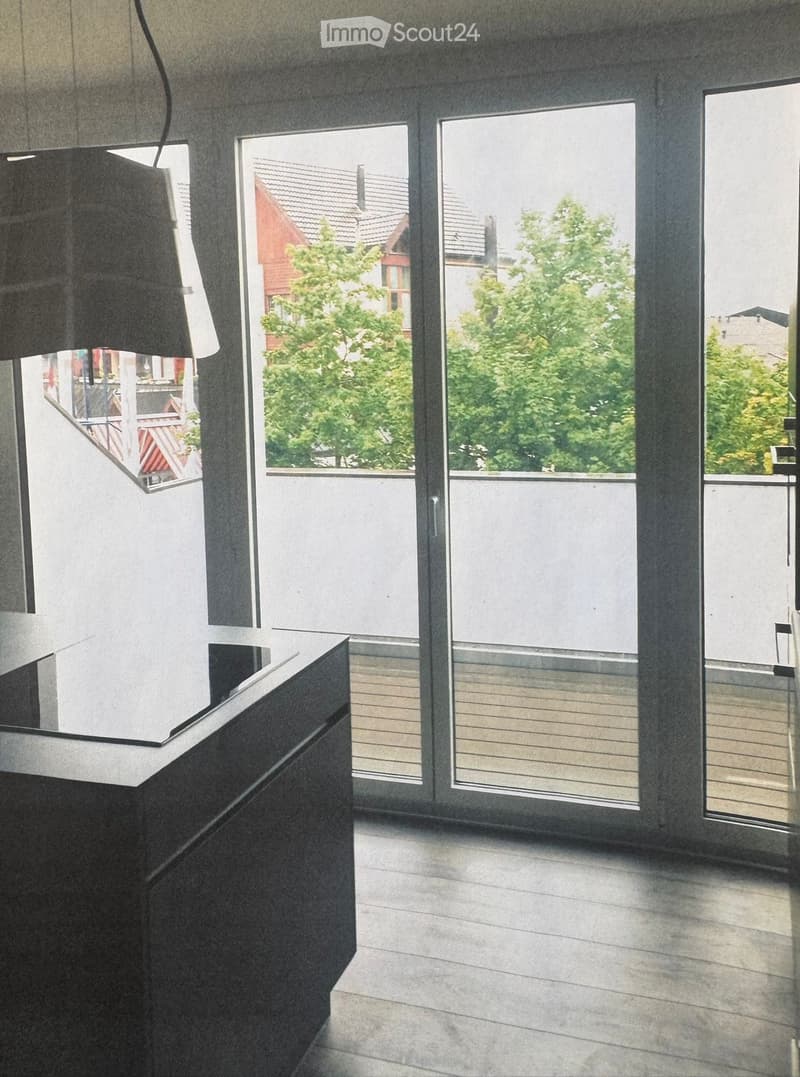 Empty room with large sliding glass doors leading to a balcony, modern minimalist design, grey walls, and a sleek black counter.