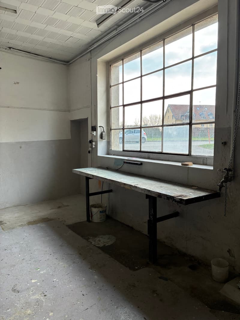Empty room with a large window, a long table, and a bucket on the floor