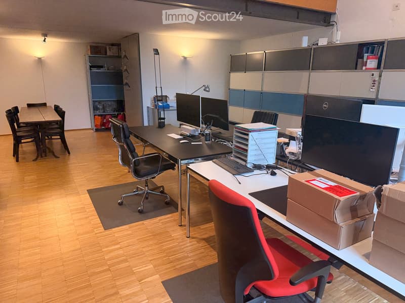 Office space with wooden flooring, desks, chairs, computer screens, and office supplies.