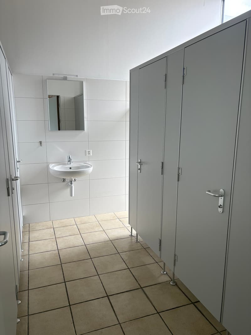 Modern bathroom with white tiled walls, beige tiled floor, a single sink with a mirror above it, and a closed cabinet door.