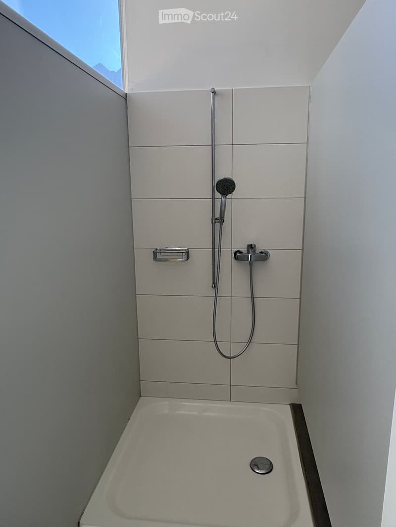 Modern bathroom with a bathtub, showerhead, and faucet. The walls are tiled in light grey, and the space features a sleek, contemporary design.