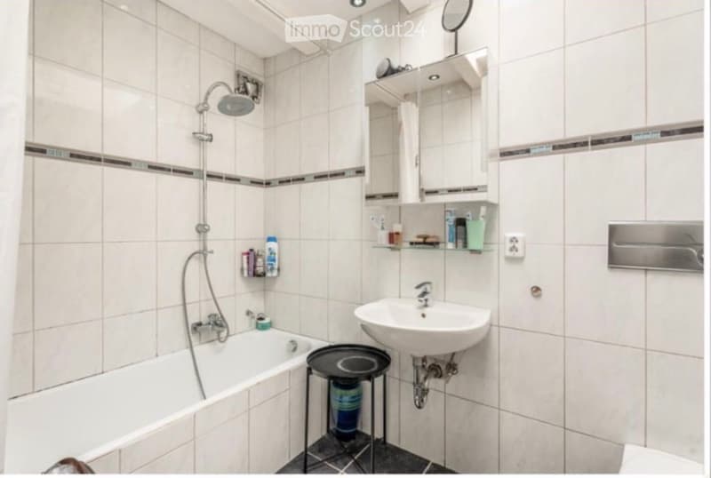 Modern bathroom with white tiled walls, a bathtub, a sink, a mirror, a shower, and a small black stool holding cups.