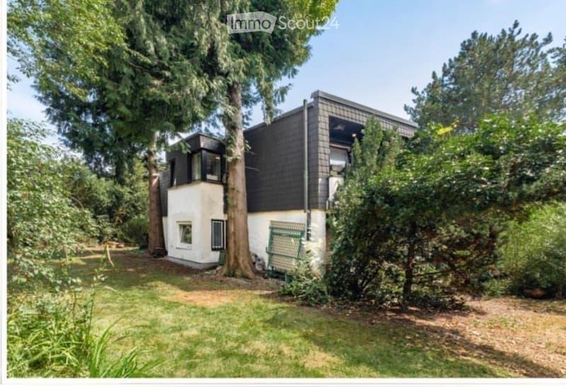 Modern two-story house with a dark roof and white walls, surrounded by trees and greenery in a serene garden setting.