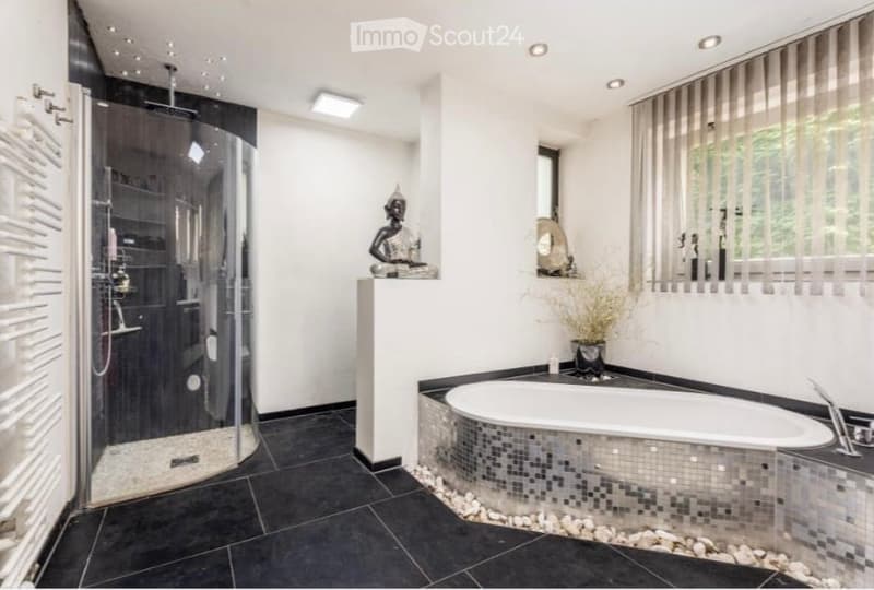 Modern bathroom with a large bathtub, glass-enclosed shower, black tiled floor, and decorative elements including a statue and a vase.