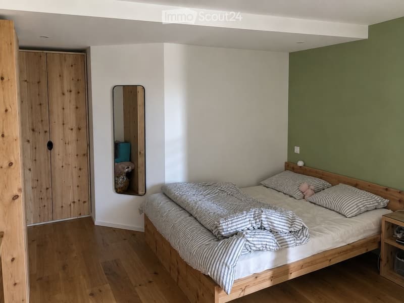 Cozy bedroom with a wooden bed, striped bedding, a wooden wardrobe, and a mirror on the wall.