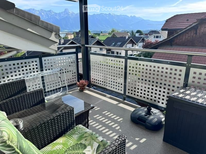 Balcony with wicker furniture, small table, potted plant, and scenic mountain view.