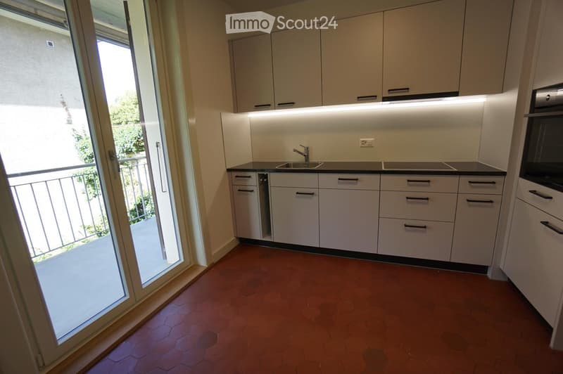 Modern kitchen with white cabinets, a sink, and an oven, featuring a large sliding glass door leading to a balcony.