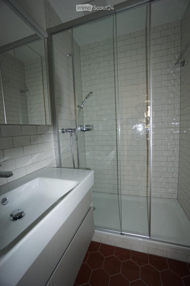 Modern bathroom with white tiles, a glass-enclosed shower, a white sink, and a mirror.