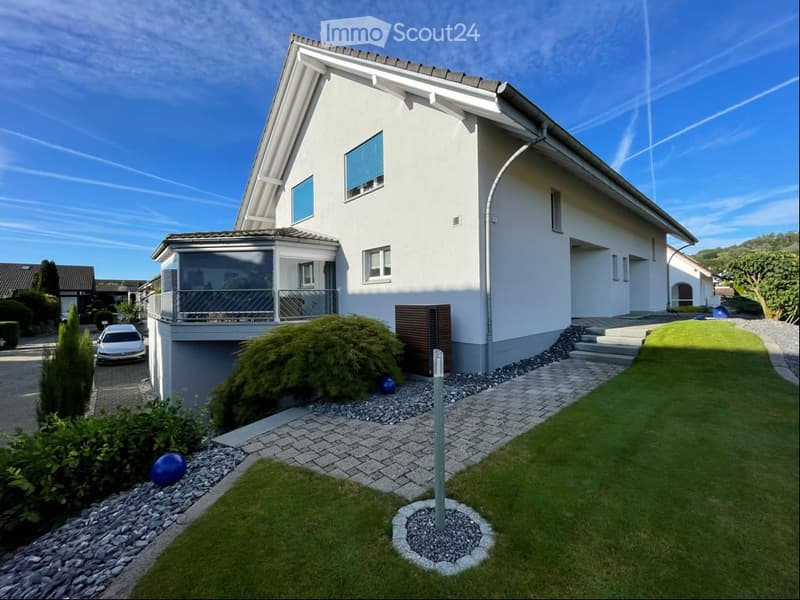 Modern two-story house with white exterior, multiple windows, garage, and well-maintained garden with a driveway and parking space.