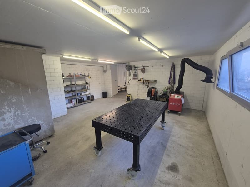 Workshop area with a large metal worktable, shelves, a chair, and various tools.