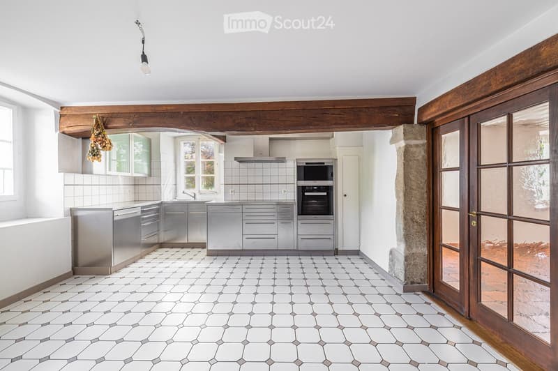 Modern kitchen with stainless steel appliances, white tiled walls, and hexagonal tile flooring. Features include a built-in oven, microwave, and a hanging light fixture.