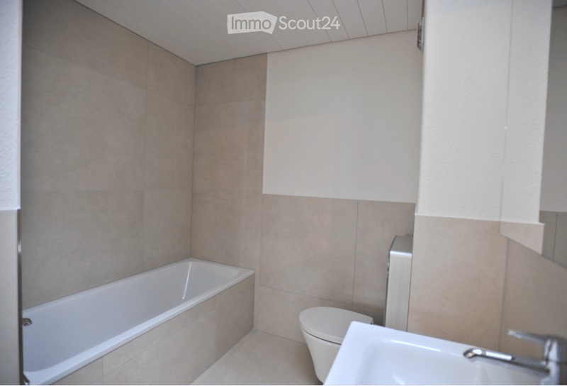 Modern bathroom with beige tiled walls and floor, featuring a bathtub, toilet, and sink.