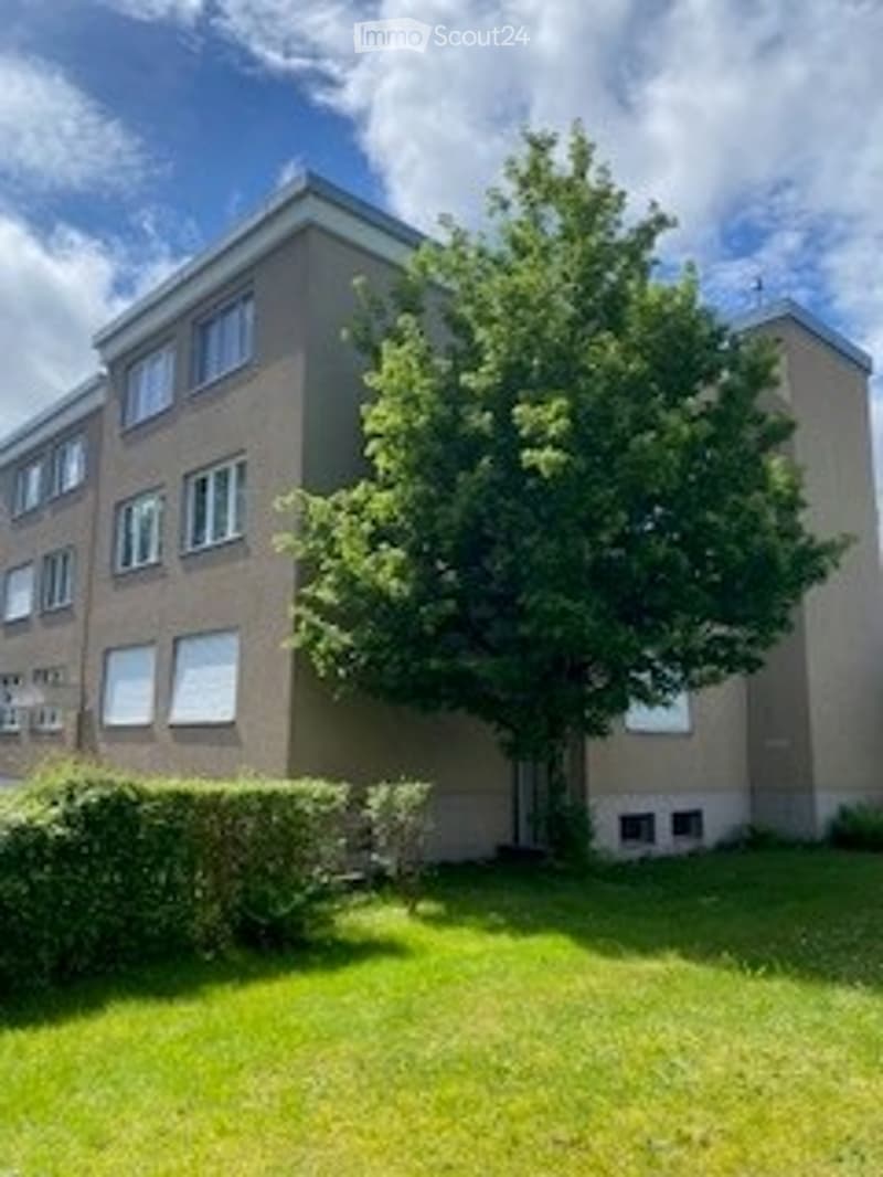 A multi-story residential building with a tree in the front yard and neatly trimmed hedges.
