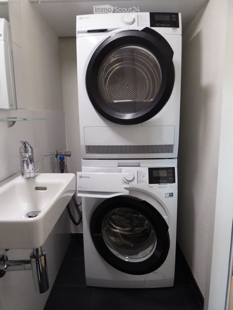Laundry area with white stackable washing machine and dryer, white sink with mirror