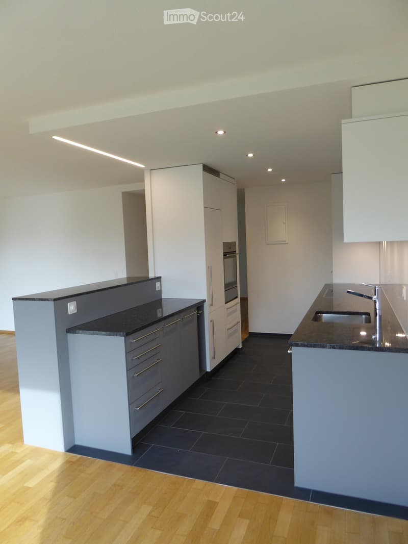 Modern kitchen with white cabinets, gray countertops, built-in appliances, and tiled flooring.
