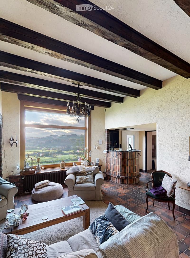 Spacious living room with wooden beams, large window, couch, coffee table, and a view of the landscape outside.