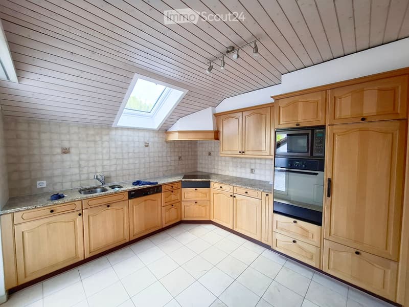 Bright kitchen with light wooden cabinets, granite countertops, and white tiled flooring. Features include a sink, faucet, oven, microwave, and range hood.