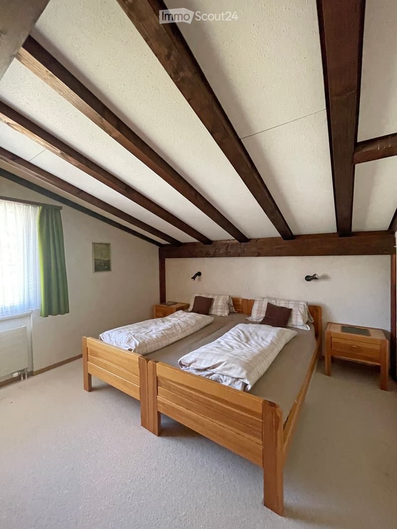 Cozy attic bedroom with wooden slanted ceilings, a double bed with pillows and blankets, two nightstands, and a small picture frame on the wall.