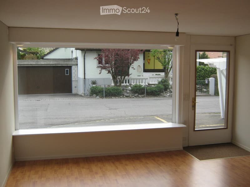 Empty room with wooden flooring, large window, and a door leading outside. No furniture or equipment present.