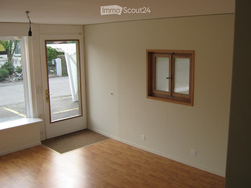Empty room with wooden flooring, white walls, a door leading outside, and a window with frosted glass panels.