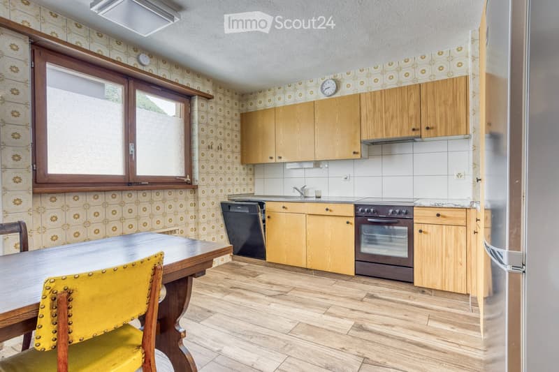 The kitchen features wooden cabinets, a stainless steel refrigerator, a dishwasher, an oven, a sink with a faucet, and a dining table with a yellow chair.