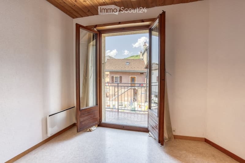 Empty room with light-colored walls, wooden trim, and a large open doorway leading to a balcony with a view of a town and surrounding landscape.