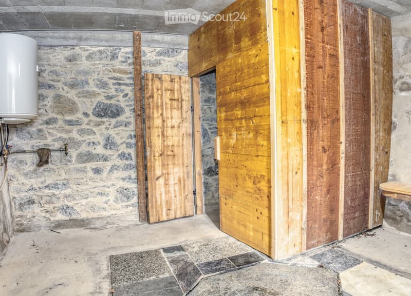 Empty room with stone walls, wooden doors, and a water heater. The floor is made of stone tiles.