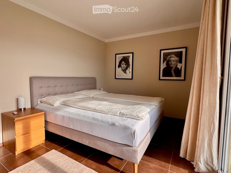 A well-lit bedroom with a double bed, nightstand, lamp, and two framed pictures on the wall.