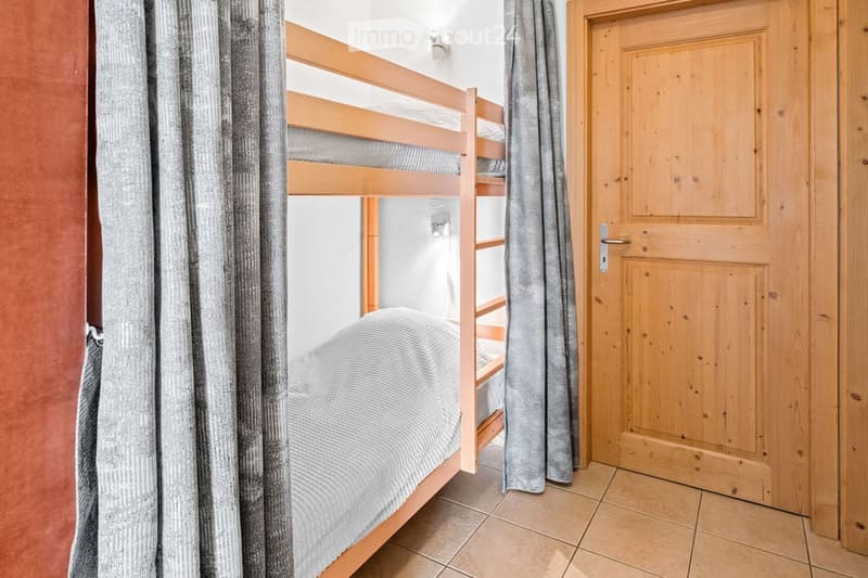 A cozy bedroom with a wooden bunk bed, grey bedding, and a wooden door with a curtain.