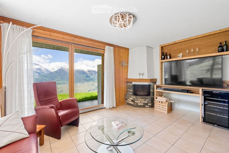 Living room with large windows offering a mountain view, a red leather sofa, a glass coffee table, a fireplace, a TV, and a floor lamp.