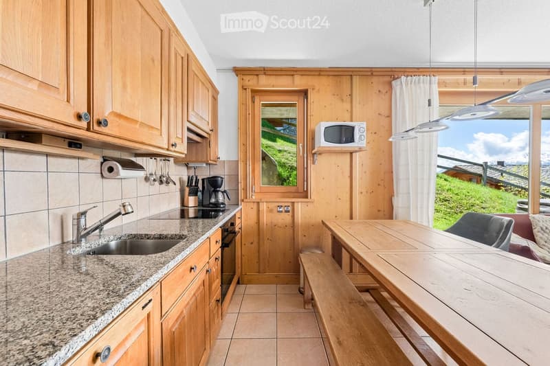 A cozy kitchen with wooden cabinets, granite countertops, a sink, microwave, coffee maker, and a dining area with a wooden table and bench.