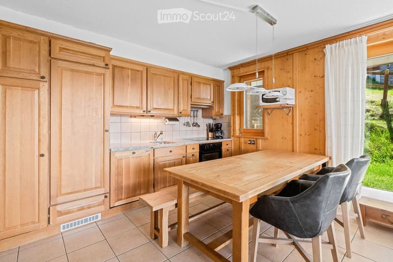 Bright kitchen with wooden cabinets, a central island, and modern appliances. The space includes a microwave, coffee maker, and a sink with a faucet. Wooden stools are placed around the island.