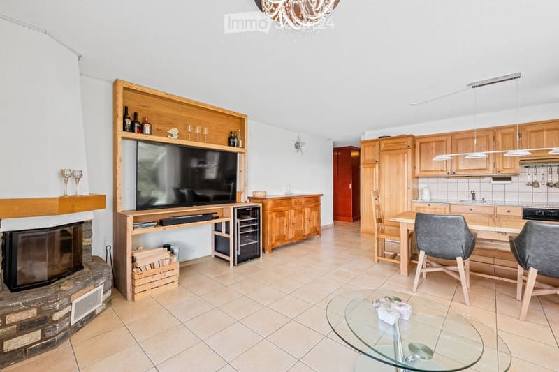 Open-plan living and dining area with a fireplace, television, wine rack, kitchen, and dining setup.
