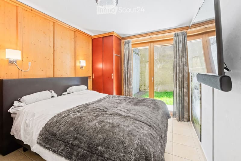 Cozy bedroom with wooden walls, a large bed with white linens and a fur throw, a wardrobe, and wall-mounted lamps.