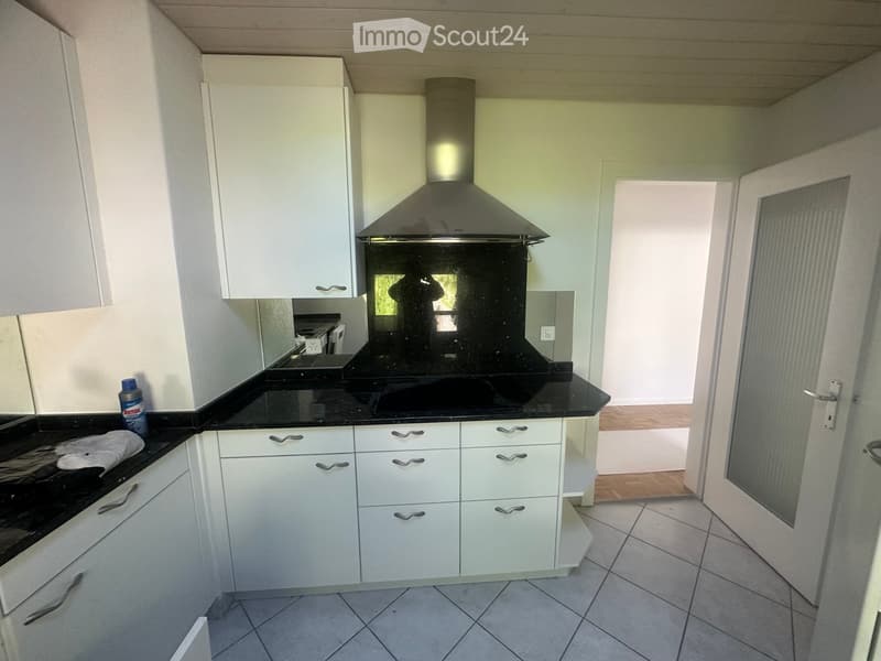 Modern kitchen with white cabinets, black countertops, and a stainless steel range hood. The floor is tiled, and a cleaning spray bottle is visible on the counter.