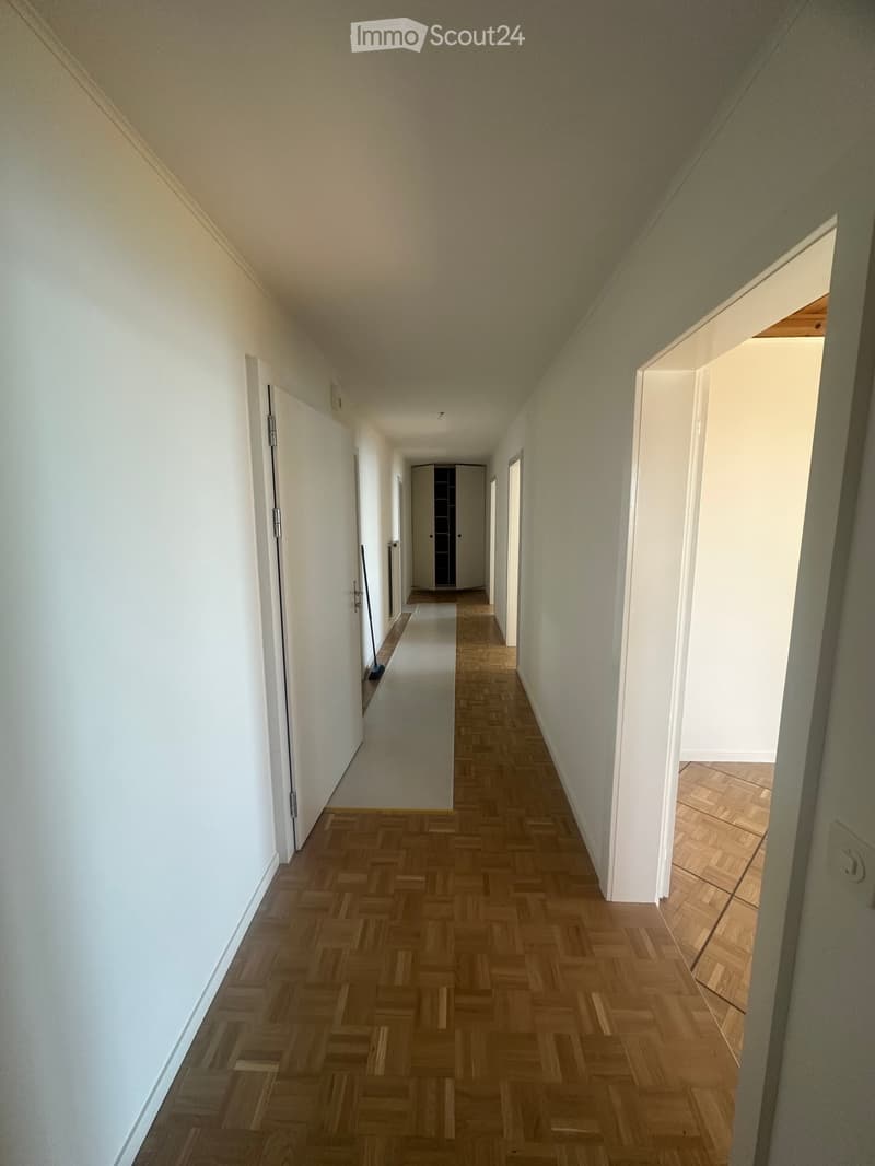 Empty hallway with wooden herringbone flooring, white walls, and several doors leading to other rooms.