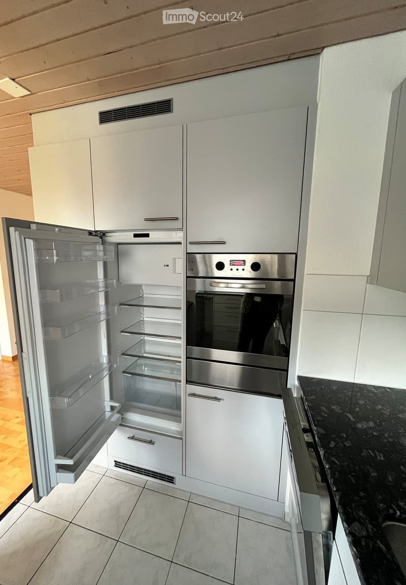 Modern kitchen with white cabinets, a stainless steel refrigerator, and a built-in oven. The refrigerator door is open, revealing empty shelves.