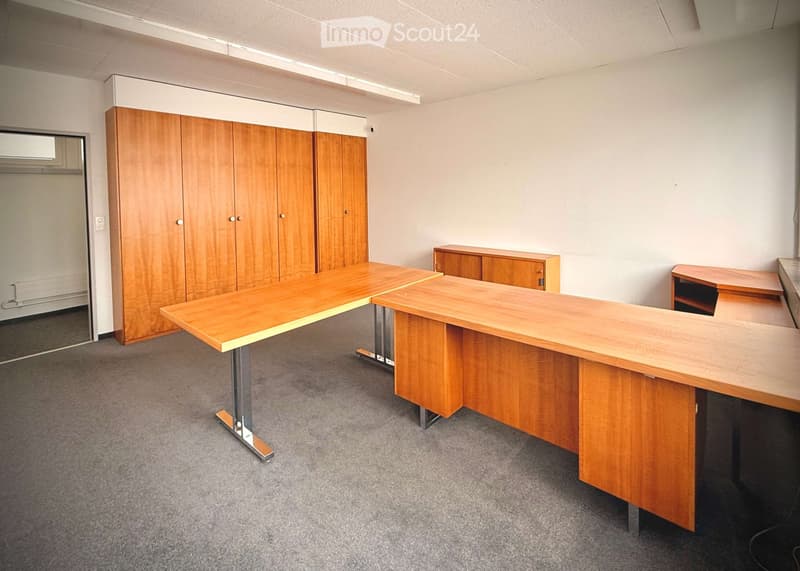 Office space with wooden tables, cabinets, and chairs arranged neatly.