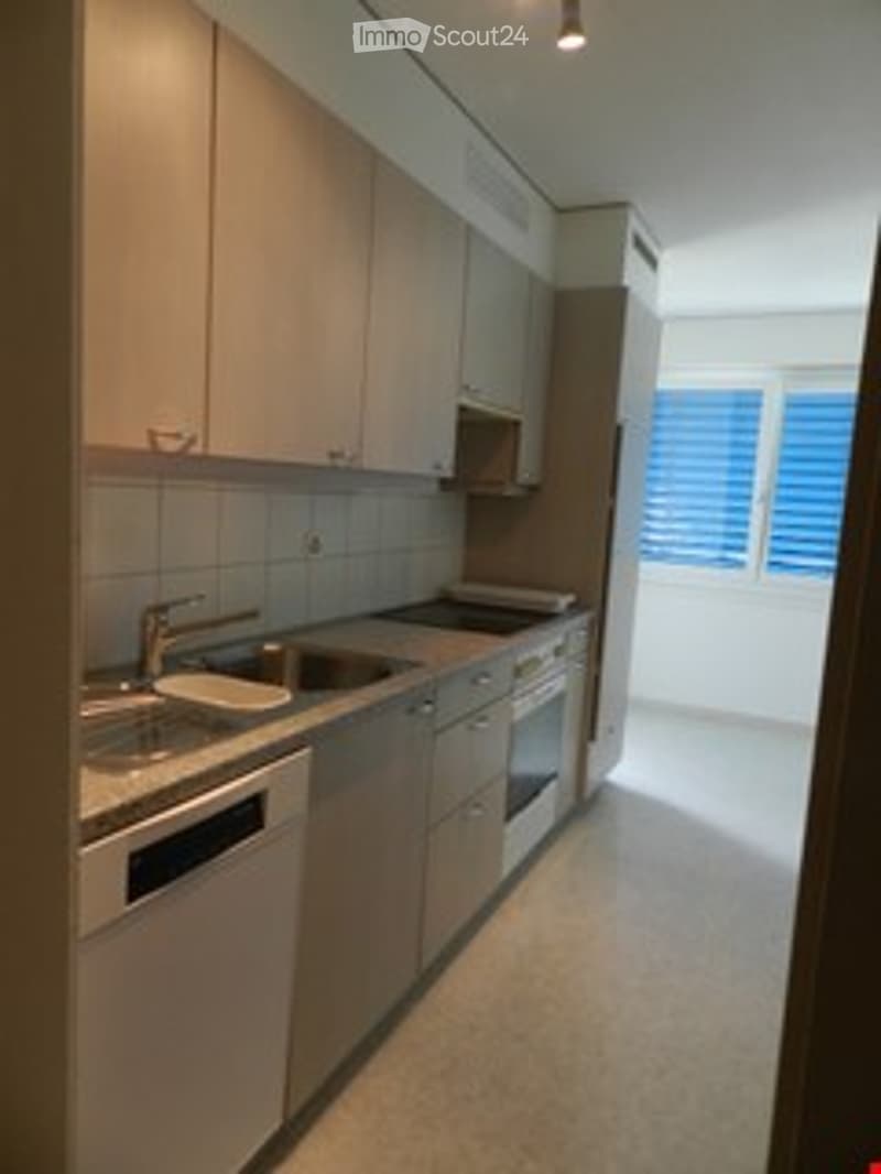 Modern kitchen with light wood cabinets, stainless steel appliances, and a large window with blinds.