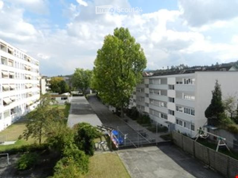A multi-story residential building complex with several apartment blocks, surrounded by greenery and a paved courtyard.
