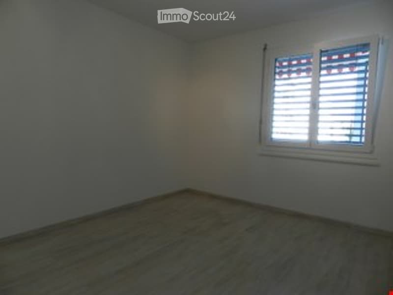 Empty room with wooden flooring and a single window with white shutters.