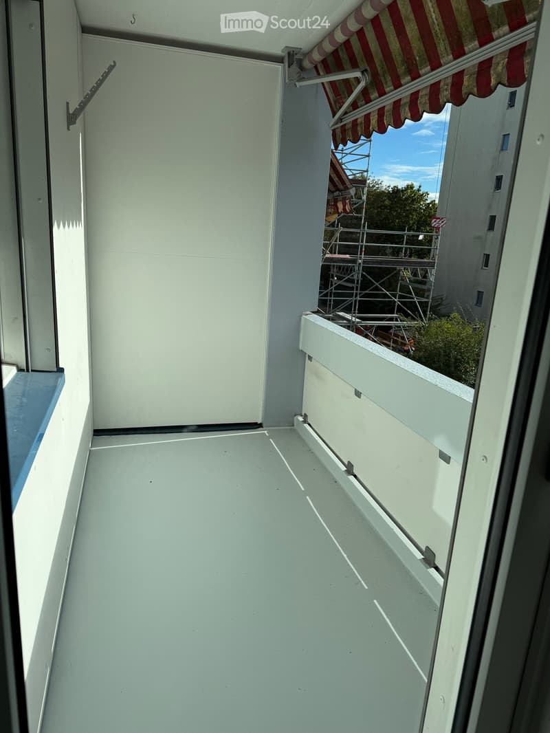 Empty balcony with white floor and walls, featuring a retractable awning and a view of a construction site.
