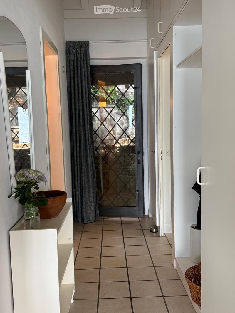 Hallway with tiled floor, white walls, a glass door with a decorative pattern, a small shelf with a vase and bowl, and a wicker basket on the floor.