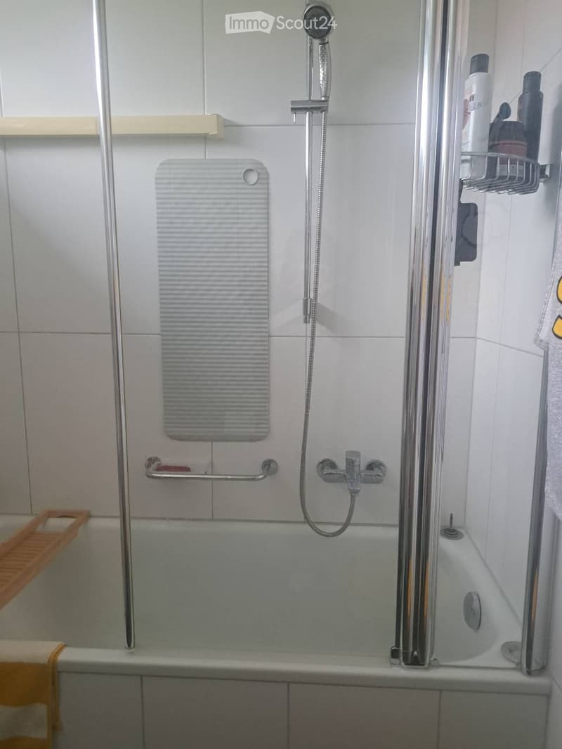 Modern bathroom with a bathtub, showerhead, shower rack, handrail, and a towel on the side.