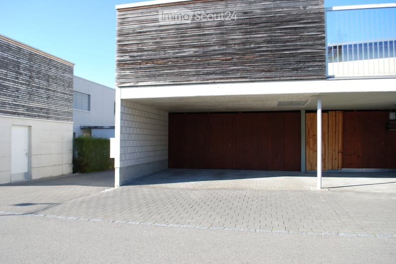 Modern two-story house with a wooden facade, large garage doors, and a covered driveway.