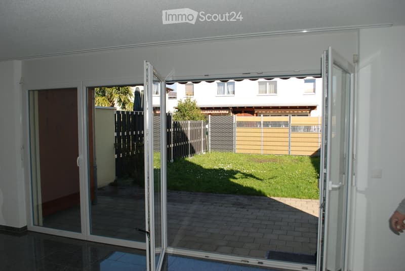 Open sliding glass doors lead to a paved patio area with a well-maintained lawn and a fenced yard beyond.