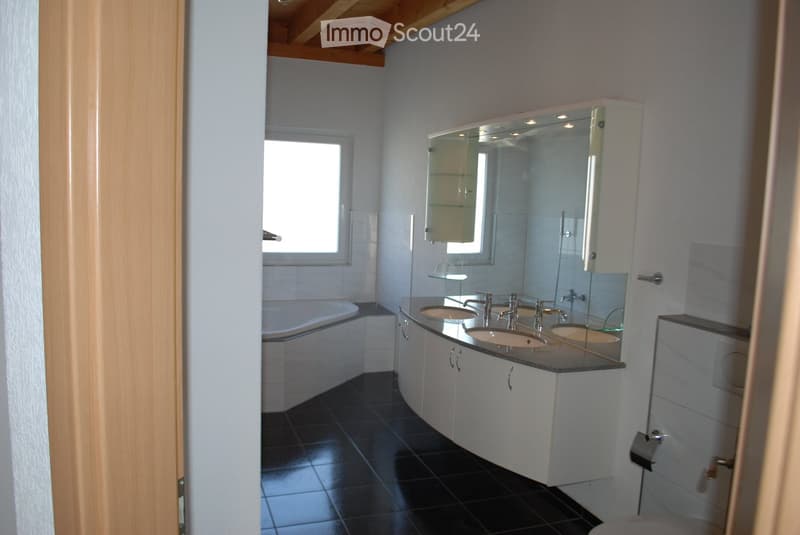 Modern bathroom with black tiled floor, white cabinets, double sink, mirror, and bathtub.