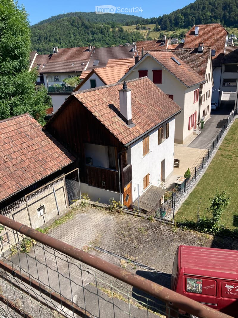 Aerial view of a residential area with multiple houses featuring red-tiled roofs, surrounded by greenery and hills in the background.