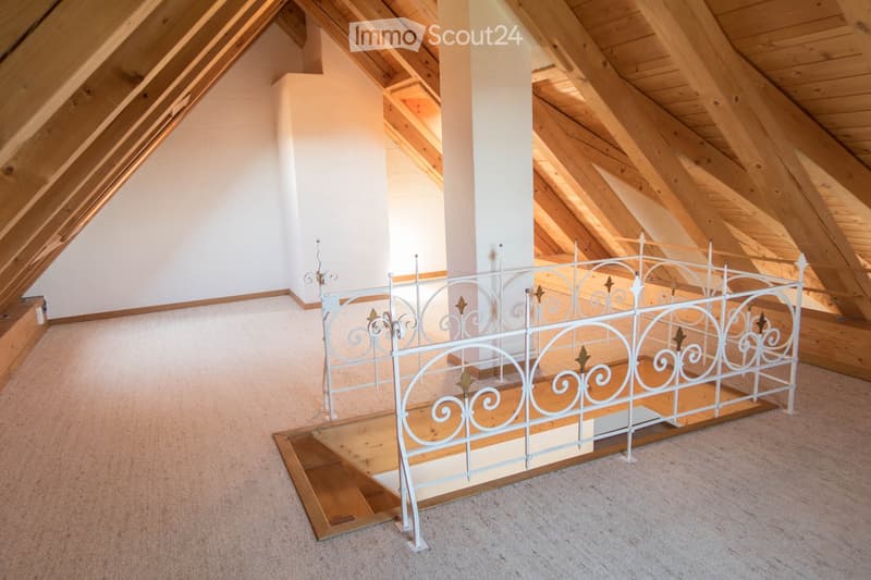 An empty attic space with exposed wooden beams, a white metal railing, and carpeted flooring.
